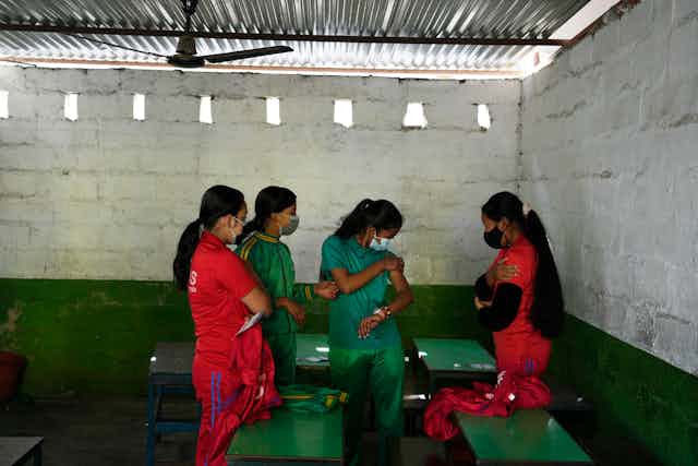 Four girls wearing red and green with face masks on stand in a school house.