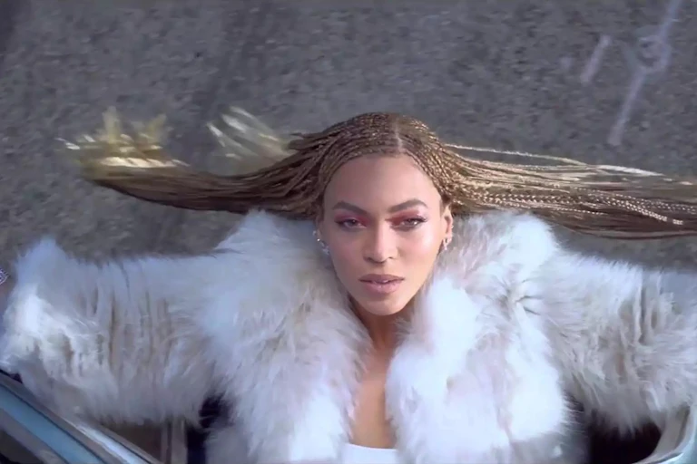 Beyoncé saca la cabeza por la ventanilla de un coche mirando hacia el cielo.
