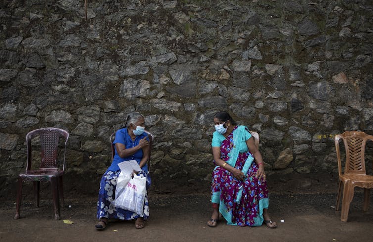 Two women sit in chairs, wearing face masks