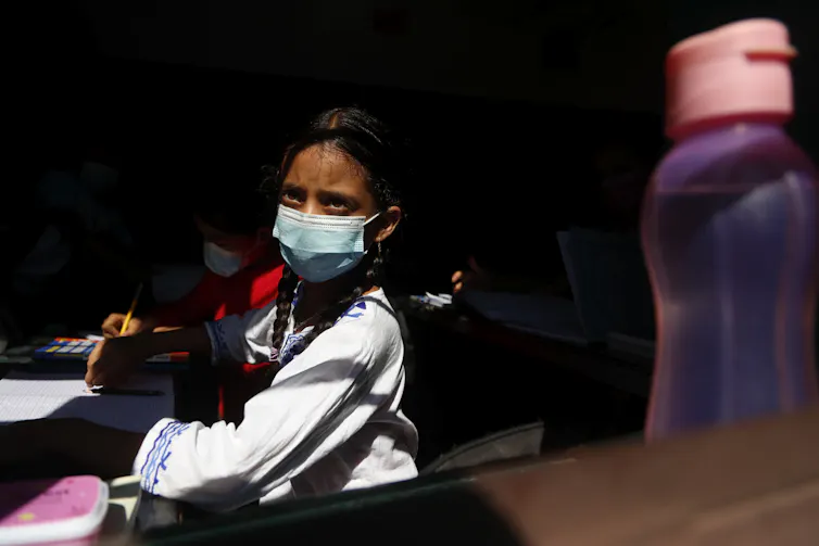 A girl in a face mask stares out a window