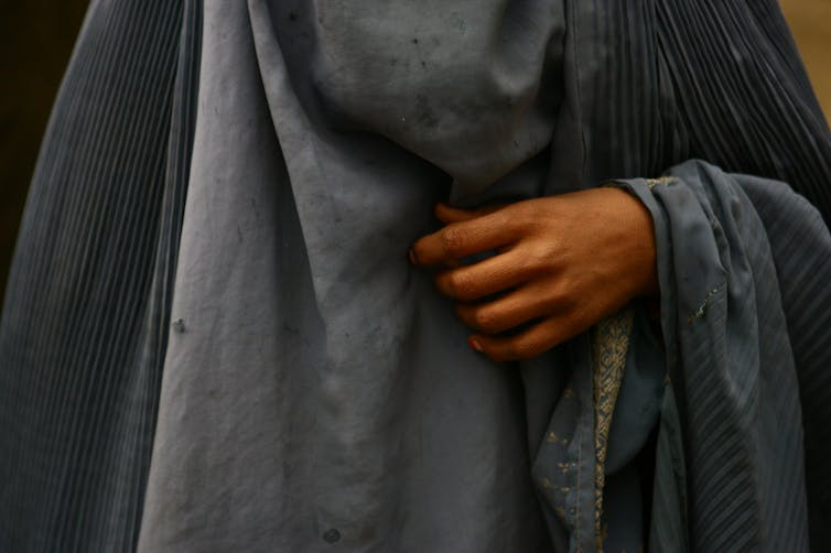 The hand of a woman in a grey burqa.