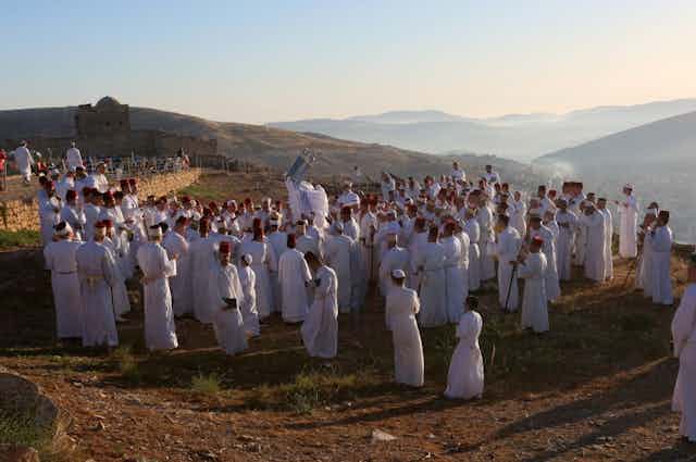 A few dozen men in white robes stand on top of a mountain.