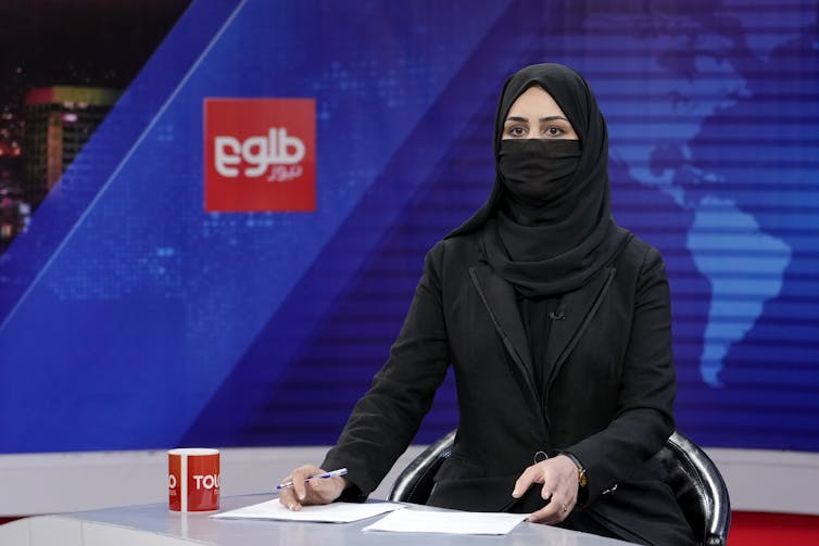 A female news anchor reads the news with her face covered.