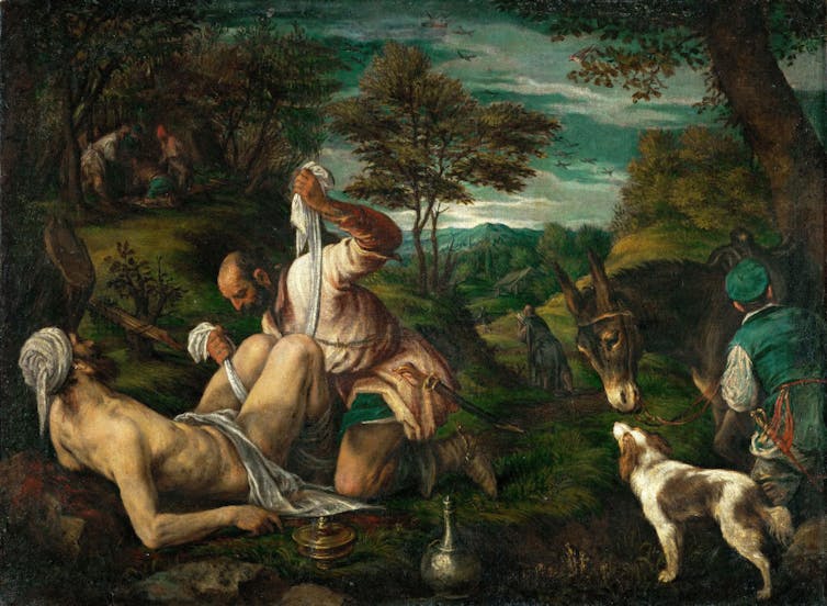 A painting shows a man bandaging the wounds of a man laying on the ground.