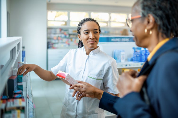 A Black female pharmacist shows Black woman some prescription medications.