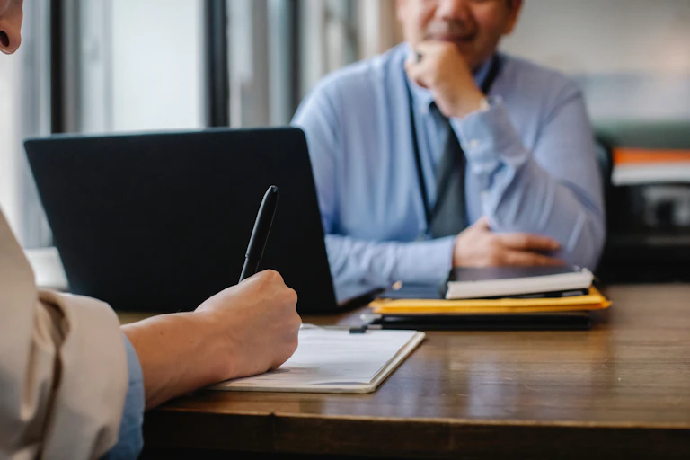 Man fills in form at desk while sitting opposite officer worker