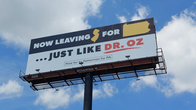 A billboard at the New Jersey/Pennsylvania border, shown against a blue sky with clouds.
