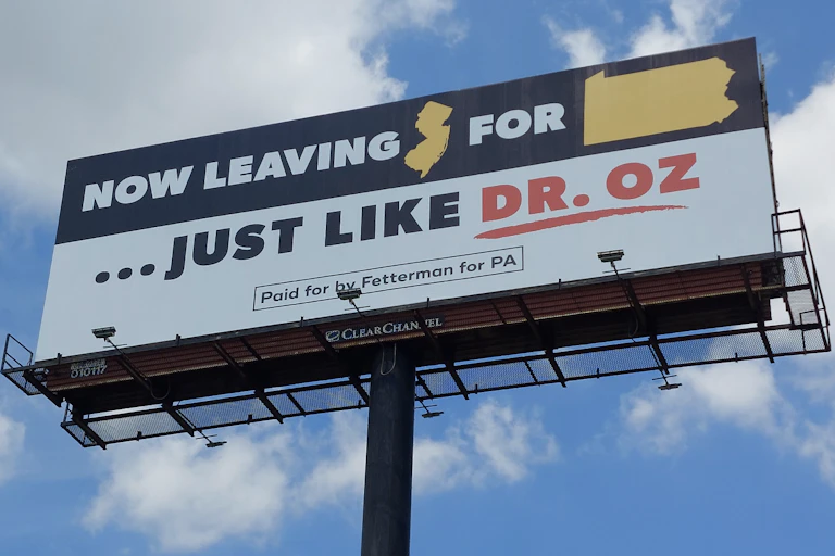 A billboard at the New Jersey/Pennsylvania border, shown against a blue sky with clouds.