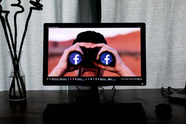 A computer screen depicts an image of a man with binoculars displaying the Facebook logo.