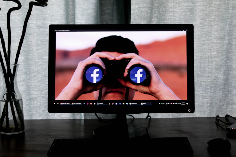 A computer screen depicts an image of a man with binoculars displaying the Facebook logo.