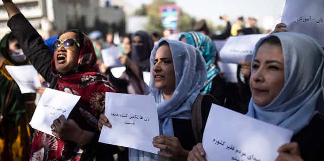 Tres mujeres sostienen carteles, una con el brazo levantado y gritando.