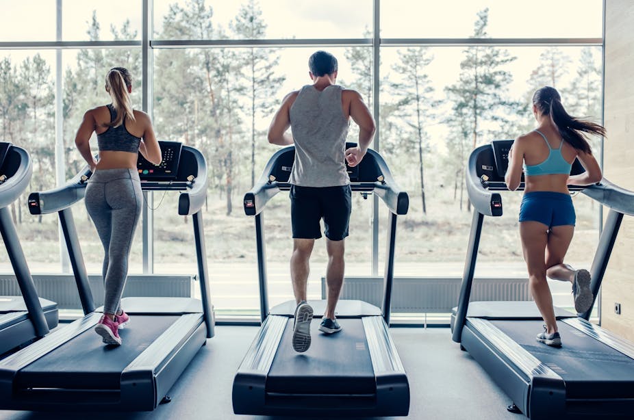 Two women and one man run on treadmills in the gym.
