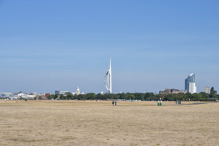 A large parched common featuring dead grass with blue sky and a large white tower in the background.
