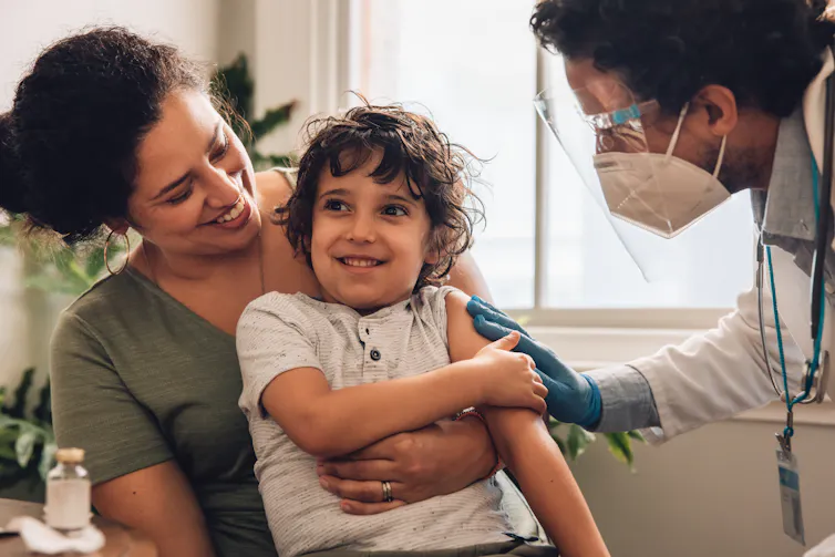 A mother holds her son on her lap while they are seen by a doctor.