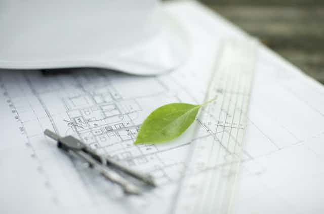 Plano de un edificio en papel y una hoja verde.
