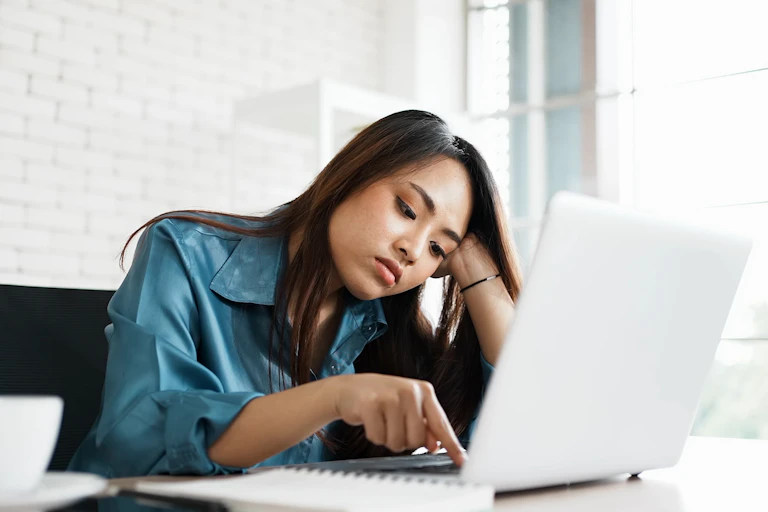 A bored young woman lazily presses a key on the keyboard of her laptop