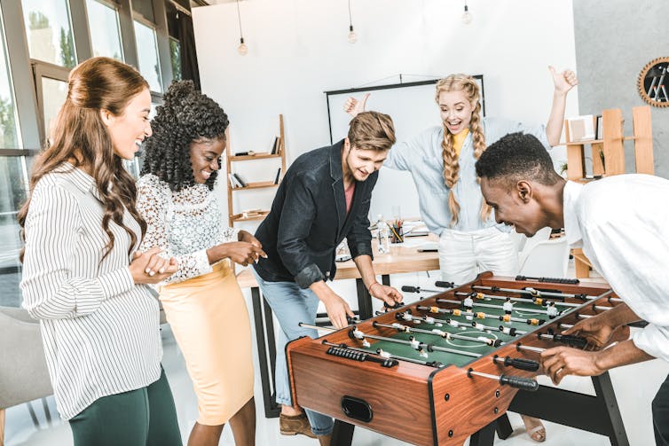 Young professionals laughing and playing table football in their office.