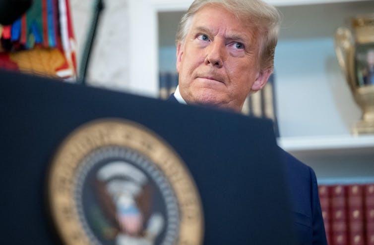 The head of a middle-aged man peers above the U.S. presidential insignia.