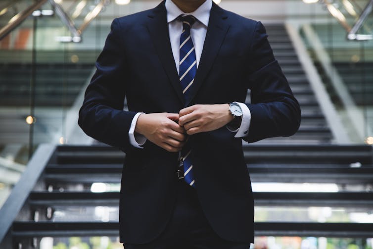 A man buttons his suit in front of a staircase - working from home concept