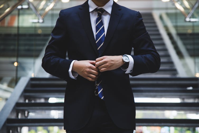 A man buttons his suit in front of a staircase - working from home concept