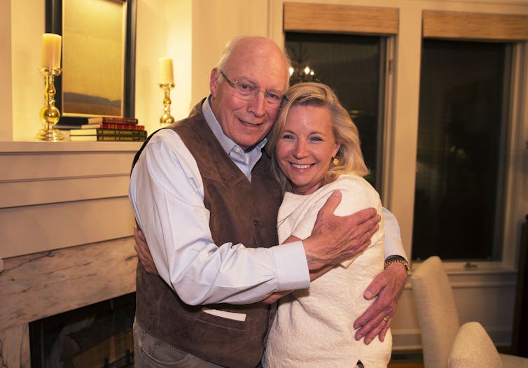 A middle-aged man hugs his daughter as they both are smiling while standing near a fireplace.