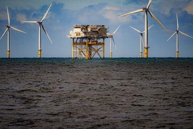 Six offshore turbines surround a support platform in ocean waters