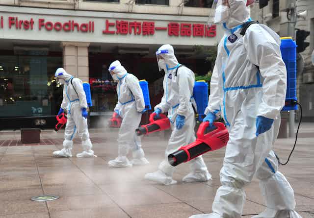 Sanitation workers wearing personal protective equipment spray disinfectant in Shanghai, China. 