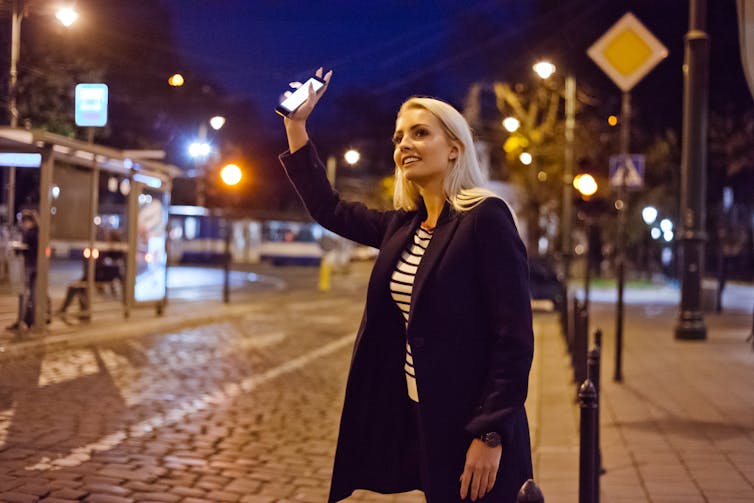 A young woman holds a smartphone in her hand and flags down a taxi