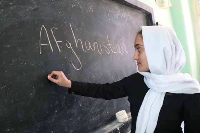 Girl writes on blackboard. 'Afghanistan' is written on the board.