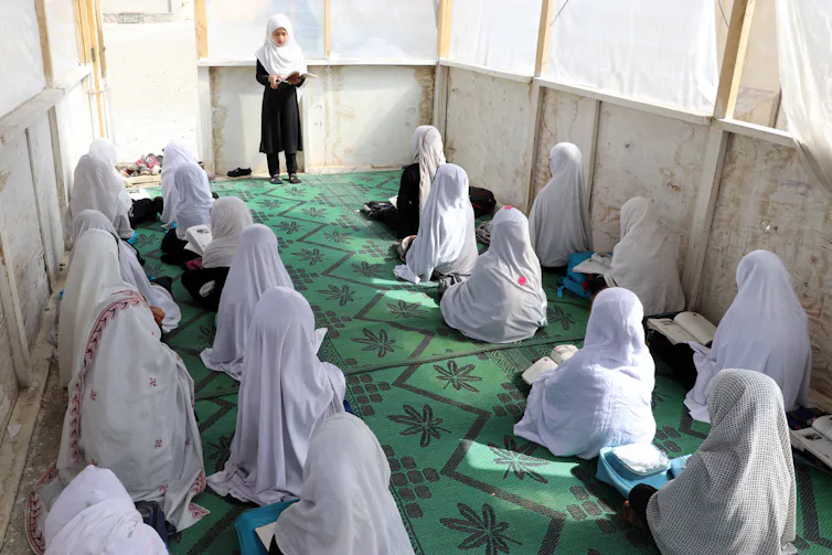 Girls sat on floor of room facing teacher