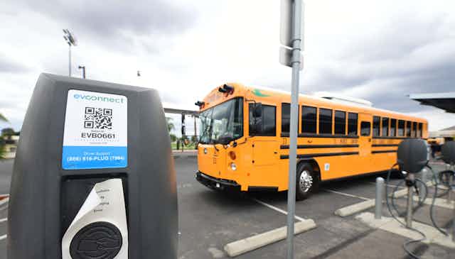 New yellow bus parked beside charging docks in a lot