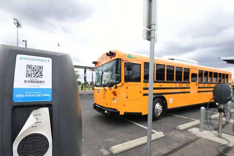 New yellow bus parked beside charging docks in a lot