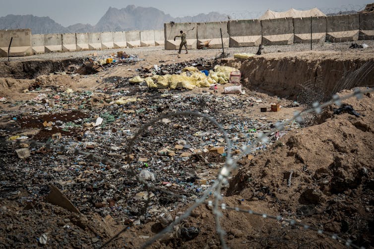 A solider is patrolling near a large pit that contains trash thrown out by U.S. military and set on fire.