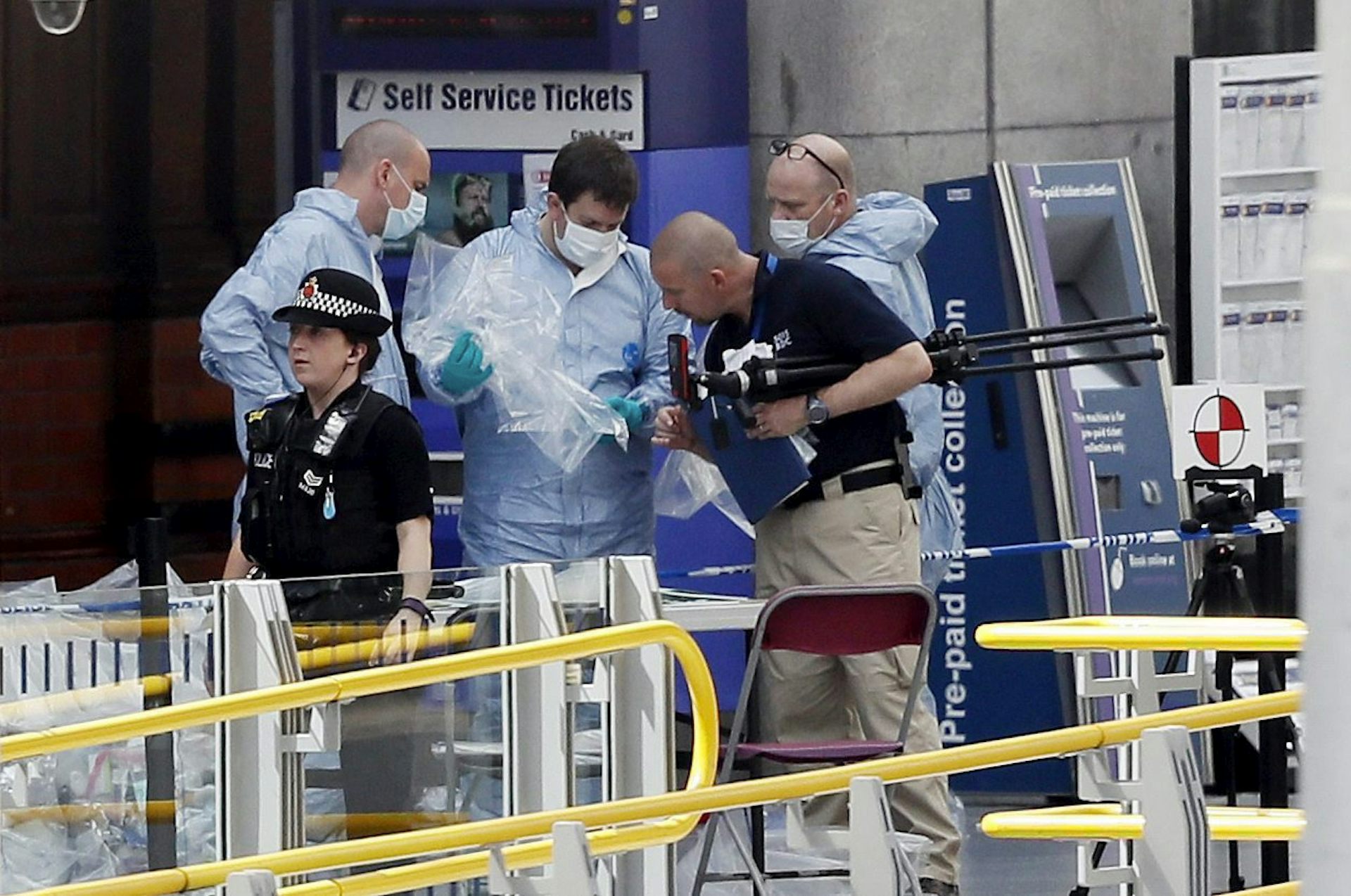 A police office walks in front of two men dressed in blue with face masks on