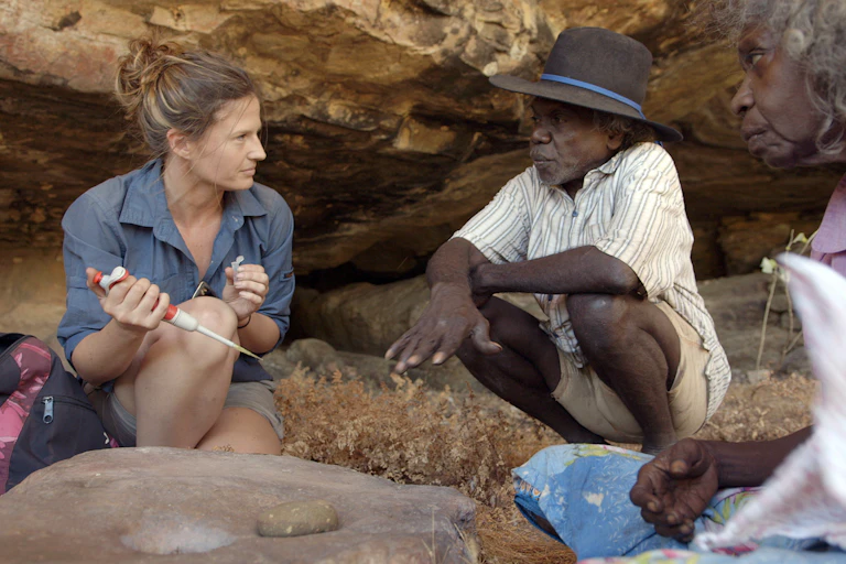 Three people sit in a cave collecting samples.One person is non-Indigenous and the other two older people are First Nations.