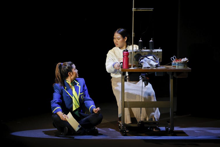 A girl on the floor, her mother at a sewing machine.