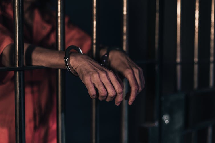 Man behind jail bars wearing hand cuffs