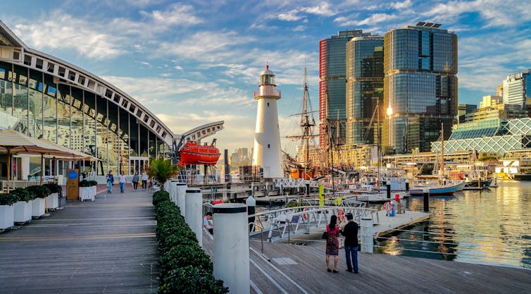 Morning at the Australian National Maritime Museum, overlooking Pyrmont Bay. Features lighthouse, moored boats and modern high-rise buildings. Some visitors around.