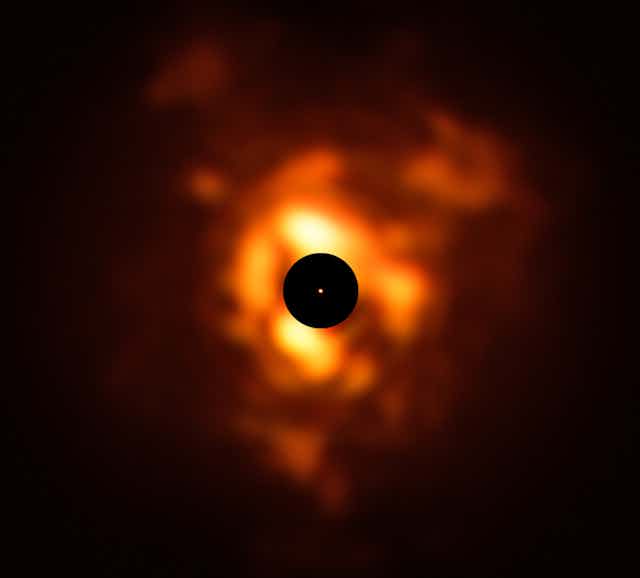 A black circle in the middle of an orange glowing dust cloud