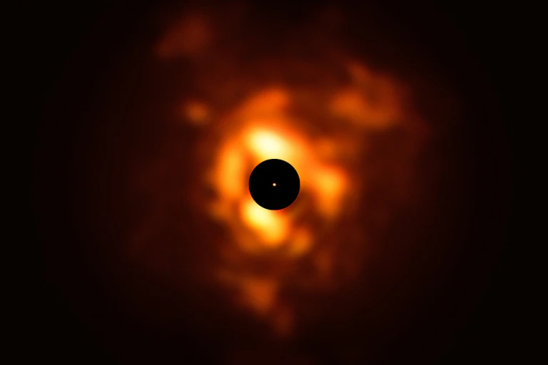 A black circle in the middle of an orange glowing dust cloud