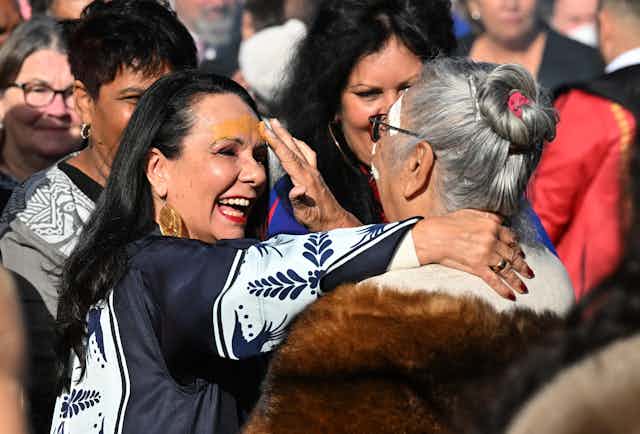 A group of First Nations politicians are together at a smoking ceremony. One of them is Linda Burney, who is having ochre put across her forehead by an Elder.