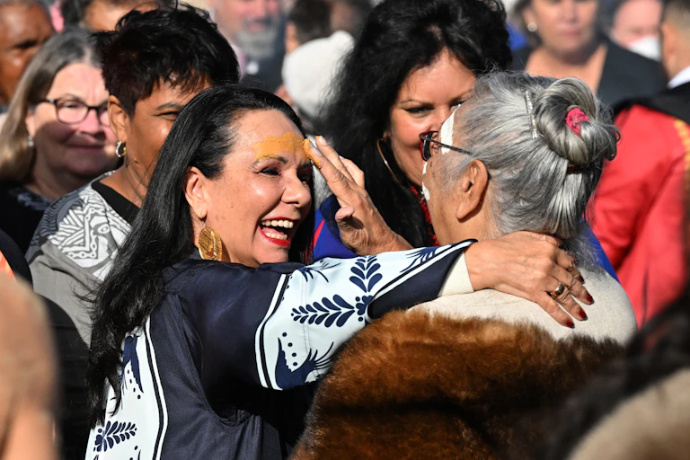 A group of First Nations politicians are together at a smoking ceremony. One of them is Linda Burney, who is having ochre put across her forehead by an Elder.