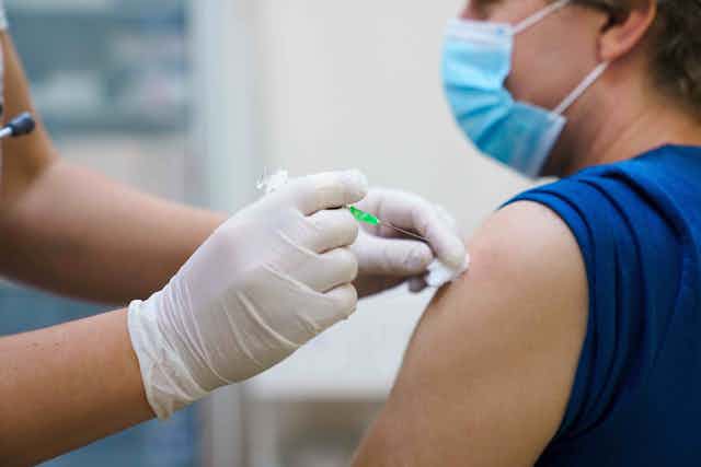 Hombre con mascarilla recibiendo una vacuna en el brazo.