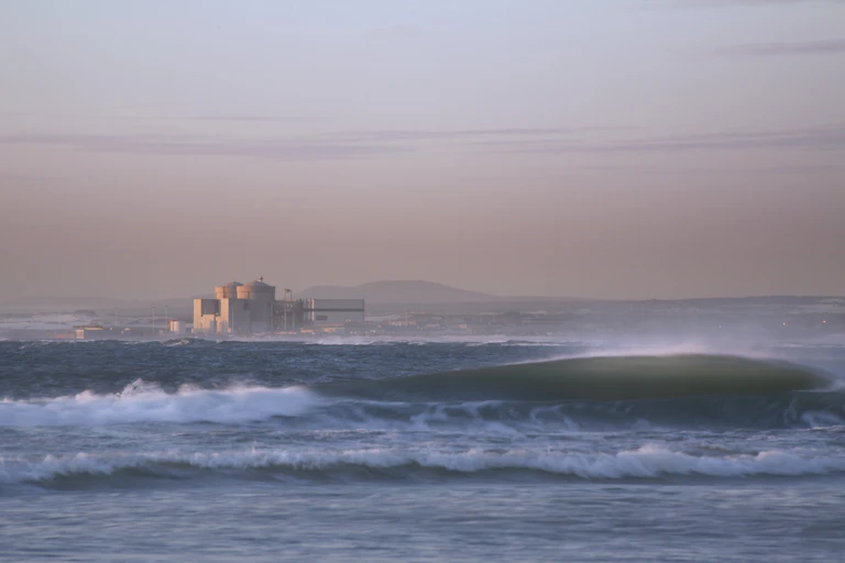 Distant view of large building, with ocean in the foreground and mountain in the background