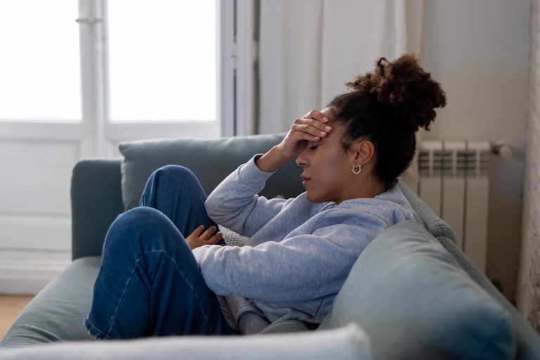 A woman sitting on a couch holding her forehead.