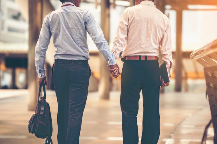 View from behind of two men in business dress walking hand in hand.