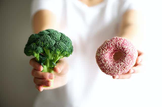 Persona sosteniendo brócoli en una mano y un donut en la otra.