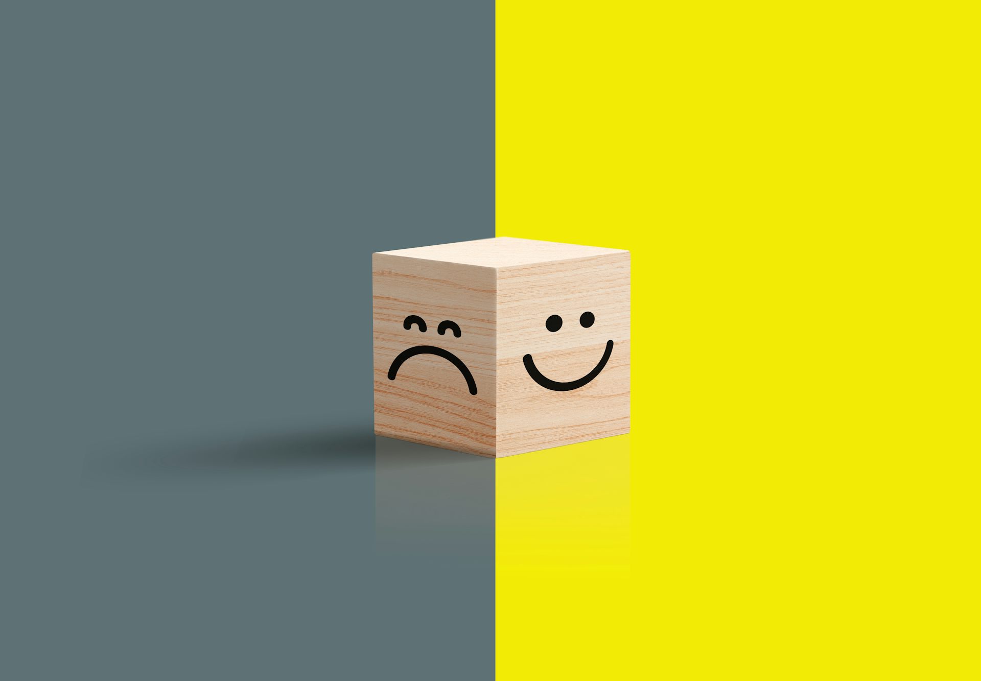 A frowny face against gray seen against a smiley face against yellow