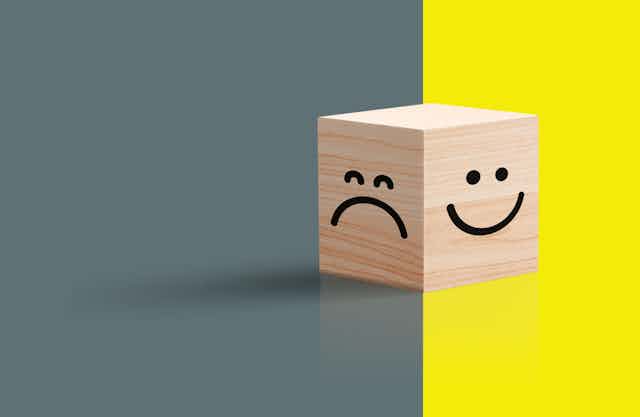 A frowny face against gray seen against a smiley face against yellow