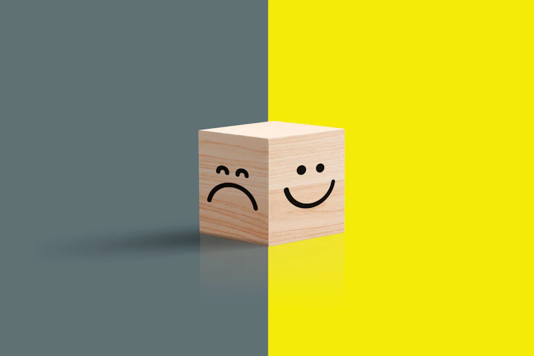 A frowny face against gray seen against a smiley face against yellow